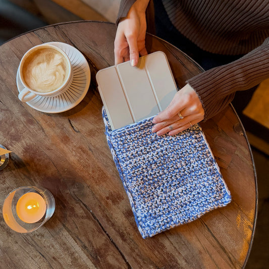 DIY-kit för iPad fodral som kallas Smooth Sleeve används av en person som lägger ner en iPad i fodralet. Fodralet har färgerna blå och vit och är placerat på en kafébord tillsammans med en kopp kaffe.