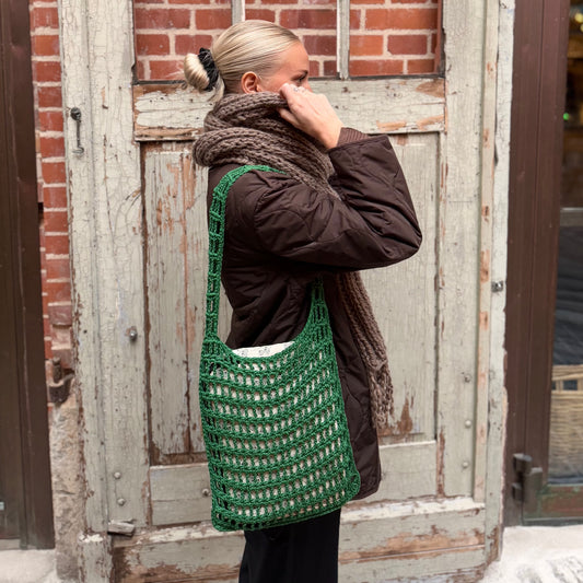 DIY-kitet för en virkad nätväska som kallas You Got It Tote (i färgen grön) bärs av en person med en brun jacka.